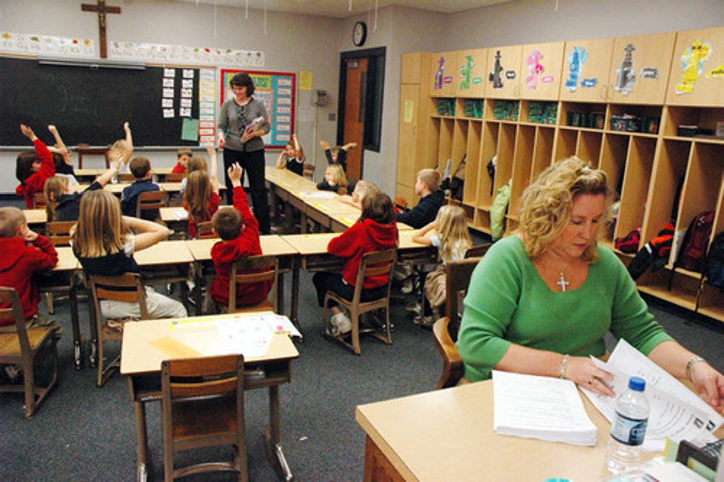 <p>a person who is employed to help a teacher in a classroom, for example giving help to children who need extra support (..tutor)</p>