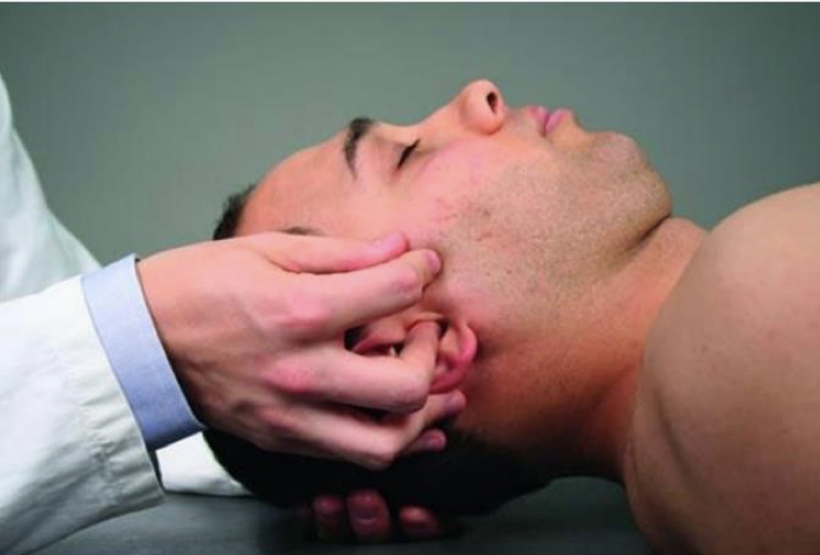 <p>Your left hand cradles the patient’s occiput.</p><p>Your right thumb and index finger grasp the zygomatic portion of the patient’s right temporal bone, with the thumb cephalad  (on top) and the index finger caudad (on bottom)</p><p>Your right middle finger rests on the external acoustic meatus of the ear.</p><p>Your right ring and little fingers rest on the inferior portion of the patient’s mastoid process.</p><p></p><p>Basically: <strong>This is the one where you put your middle finger in their ear</strong></p>