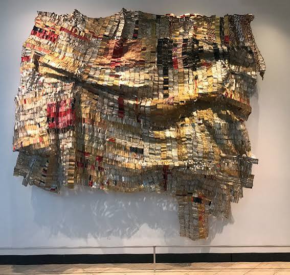 <p>A contemporary installation hanging like a tapestry, constructed from thousands of flattened, recycled aluminum liquor bottle caps. It links modern consumer trade straight back to the historical realities of African slave trade routes.</p>