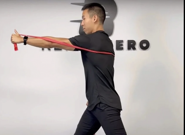 <p>loop band around each wrist. Pt pushes out into the band to</p><p>create tension and then lifts both arms OH while maintaining the tension.</p>